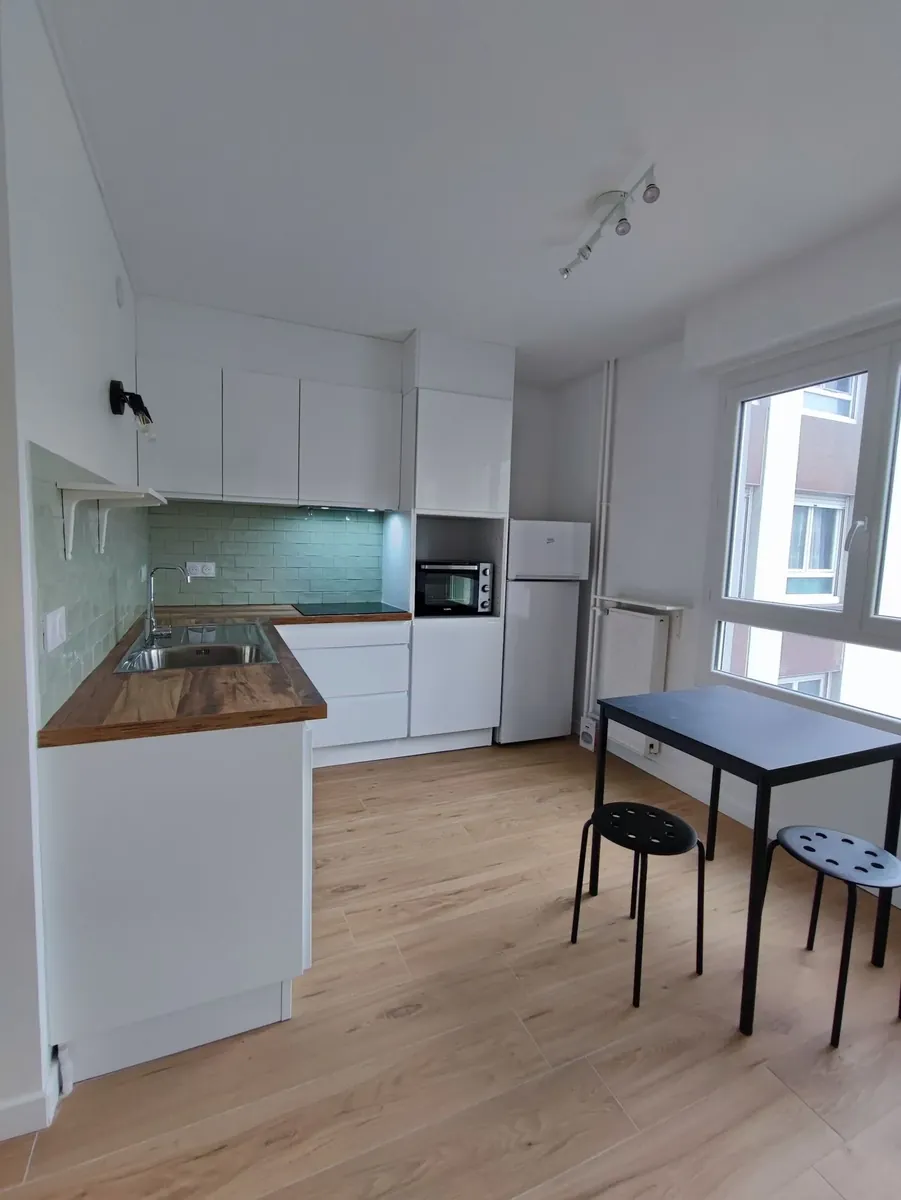Cuisine ouverte aux meubles blancs, plan de travail en bois, crédence verte et sol clair